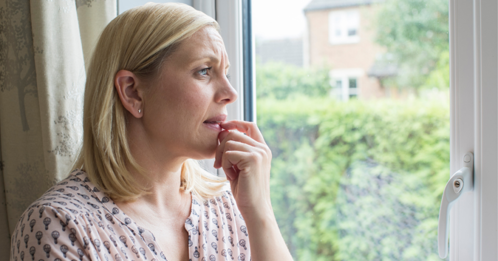 concerned woman who is a victim of domestic abuse looking out window of home